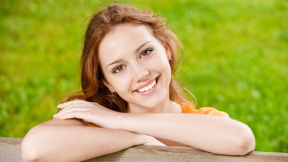 Women smiling with arms crossed on a fence outside